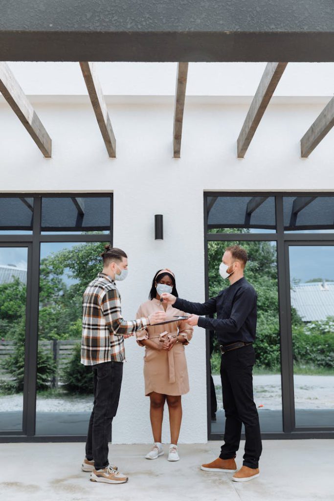 Real estate agent handing keys to clients outdoors, showcasing a successful property transaction with safety measures.